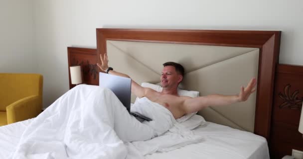 Man Stretches Arms Sides Finishing Work Laptop Bed White Blanket — ストック動画