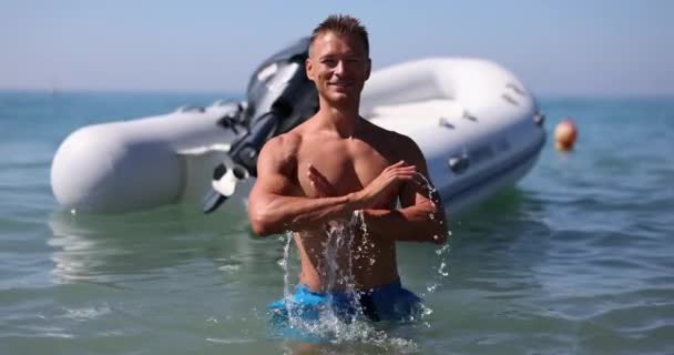 Ένας Χαρούμενος Αθλητικός Άνθρωπος Στέκεται Στη Θάλασσα Κοντά Μια Λαστιχένια — Αρχείο Βίντεο