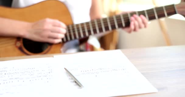 ノートとペンはテーブルの上にあり クローズアップ スローモーションです 男はギターを演奏し 音楽を構成し 浅い焦点 — ストック動画