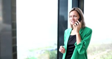 Ofiste pencerenin yanında duran bir kadın telefonla konuşuyor, yakın plan. İş yerinde mutluluk, çalışan.