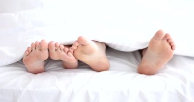 Erkek ve kadın ayakları beyaz bir battaniyenin altında, yakın plan. Cinsel ilişkiler, otelde rahat bir yatak.