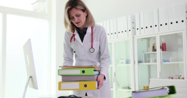 診療所の職場で文書ファイルのスタックを持つ看護師 医療記録と患者の履歴 — ストック動画