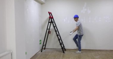 Sert şapka üreticisi merdiven üzerindeki büyük kasları gösteriyor. Usta mühendis güçle övünür
