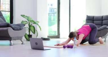 Odaklanmış motivasyonlu kız dizüstü bilgisayarı açık ve eğik bir şekilde yerde oturuyor. Güçlü fiziksel olarak sağlıklı bir kadın ve çevrimiçi fitness ve esnek yoga.