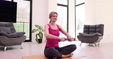 Elinde dambıllarla evde egzersiz yapan gülümseyen genç bir kadın. Spor sağlık ve spor