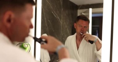 Dişlerini fırçalayan genç bir adamın ayna yansıması. Sağlıklı gülümseyen, dişlerini fırçalayan ve sabah rutinini yapan yakışıklı bir adam.