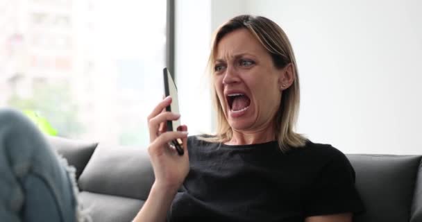 女性は男性から分離メッセージを受け取ります 自宅のソファーで電話で話しているショックを受けた女性 — ストック動画