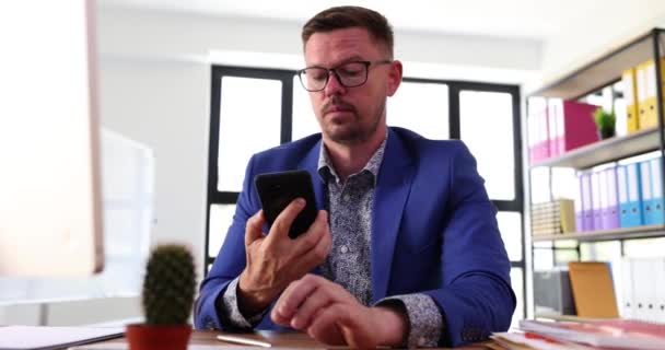 Bonito Empresário Sorridente Está Sentado Mesa Escritório Segurando Smartphone Conversando — Vídeo de Stock