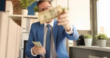 Genç mutlu iş adamı dolarları sayıyor ve onları ofis 4K filminde dağıtıyor. Kârlı iş anlaşmaları kavramı