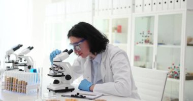 Bilimsel amaçlar için hasatı inceleyen odaklanmış erkek bilim adamı. Öğrenci adam, laboratuarında tahıllı cam parçalarıyla masada oturuyor ve mikroskoba bakıyor.