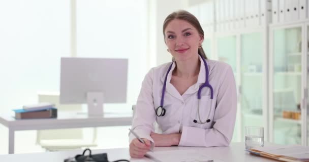 クリニックで自信のある若い女性医師の肖像画 笑顔の女性セラピストやクリニックの医学雑誌で執筆 — ストック動画