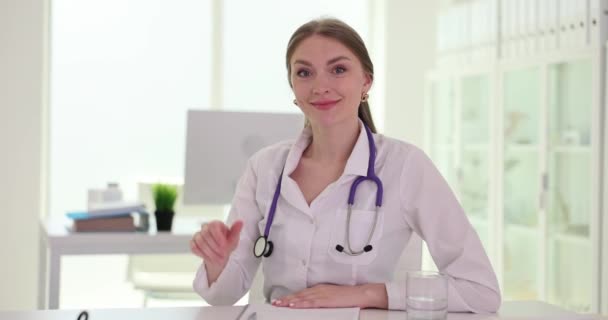 Doctor Waves Hand Smiles Looks Camera Sits Table Clinic Telemedicine — Stock Video