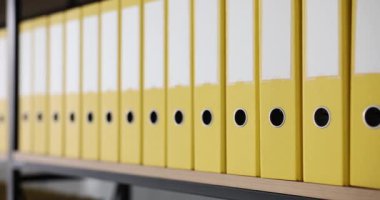 Raflarda klasörleri ve belgeleri olan sarı klasörler. Modern ofiste düzenli dizin yapısı ve arşiv