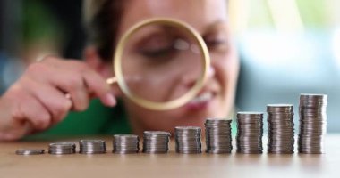 Büyüteç kullanan bir iş kadını yükselen para yığınlarını inceliyor. Finansal kar ve nakit geliri artışı