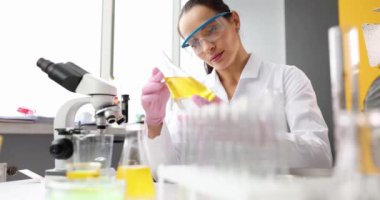 Laboratuvardaki kadın bilim adamı şişedeki sıvıya yakından bakıyor. Yağ kimyasal analizi