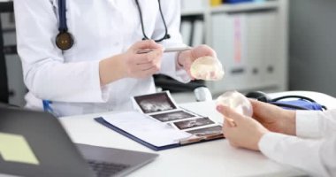 A doctor and a woman hold a silicone breast implant, close-up, slow motion. Plastic surgery, breast augmentation