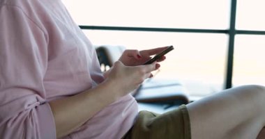 A woman in shorts uses a smartphone in the waiting room, close-up. Travel, airport. Waiting in the lounge area of the station