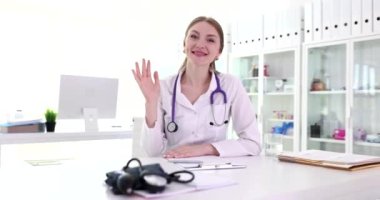 Web kamerasına bakıp klinikte el sallayan mutlu kadın doktor. Hastaneden hastayla konuşan bir tıp çalışanı.