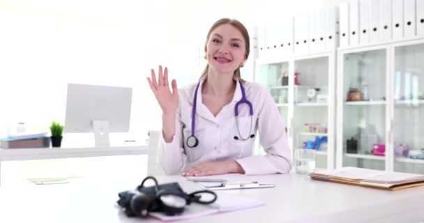 ハッピーな女性医師がウェブカムを見て 診療所で手を振っています 病院からオンラインで患者と話す医療従事者 — ストック動画