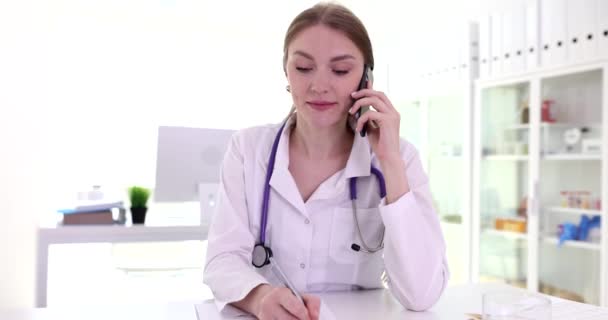 Женщина Врач Проводит Телефонные Консультации Пациента Онлайн Делает Заметки Заполняет — стоковое видео