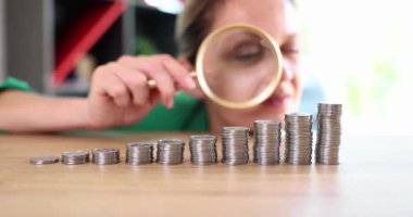 Businesswoman looking through magnifying glass at coins in ascending order 4k movie slow motion. Business earning strategy concept