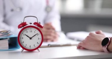 Doktor hastayla ön planda kırmızı alarmlı bir saat ile görüşüyor. Tıbbi çalışma günü konsepti