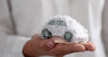 Kadın oyuncak arabayı plastik ambalaj filmiyle tutuyor. Araba sigortası kavramı