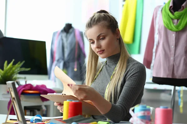 Moda tasarımcısı stüdyoda bir renk tasarımı üzerinde çalışıyor. Çalışma masasında oturan güzel bir kadın iş kıyafetleri skecine bakıyor.