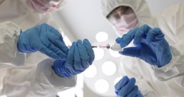 Eldivenli ve maskeli iki doktor aşıyla ya da şişeden ilaç alıyor. Temel ilaç konsepti