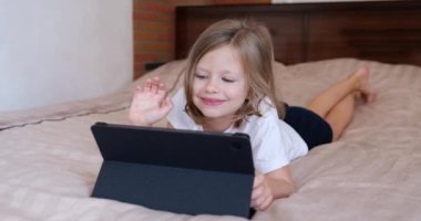 Küçük kız elini dijital tablete sallıyor ve video bağlantısı ile iletişim kuruyor. Çocuklar için mobil uygulama kavramı