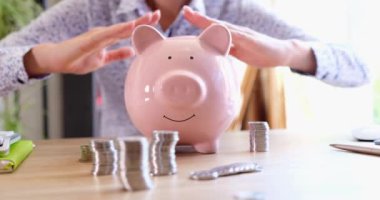 Business woman making roof from her hands over piggy bank with coins closeup 4k movie. Investment insurance concept