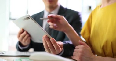 Bayan ofis çalışanı, masadaki aletli erkek meslektaşına proje görevlerini açıklıyor. Müdür, genç çalışanlara ağır çekimde talimatlar veriyor.