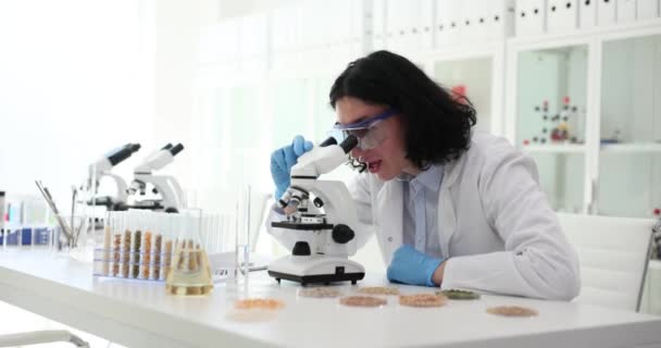 男性科学者は 実験室の職場で顕微鏡を介して重要な発見をする 失敗した実験の遅い動きのために欲求不満の長い髪のスペシャリスト — ストック動画