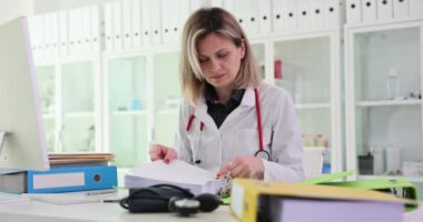 İlgili kadın doktor, hastanedeki işyerindeki müşterilerle ilgili bilgilerle belgeleri inceliyor. Ağır çekimde önemli meslek ve evrak kavramı