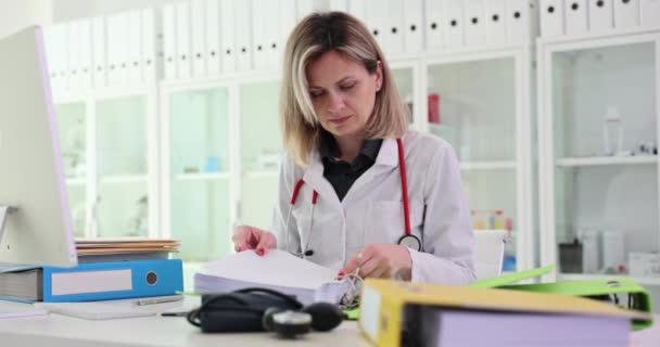 注意深い女性医師は 病院の職場のクライアントに関するデータを持つ文書を検査します テーブルのスローモーションにおける重要な職業と書類の概念 — ストック動画