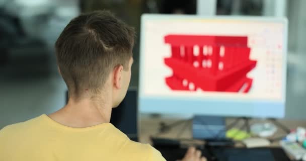 男性アーキテクトは 部屋のぼやけた背景にコンピュータ上で赤い家3Dモデルを開発しています 建築構造のイノベーションと開発の概念 — ストック動画