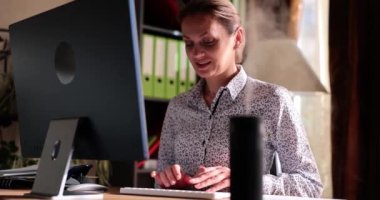 Kadın serbest çalışan, ofisteki bilgisayardan nemlendiriciyle çalışıyor. Bluzlu bayan işçi yavaş çekim için online toplantıya hazırlanıyor.