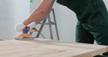 İş elbiseli marangoz ofis masasında marangozluk yapıyor. Düz çekimde parlak ışıklı odada ahşap cilası kullanan erkek.