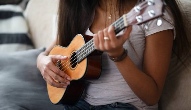 Ukulele tutan ve çalmayı öğrenen Latin kadının yakın çekimi. Genç bir bayan oyun oynarken egzersiz yapıyor. Müzikal tahta enstrüman. Müzik ve sanat konsepti