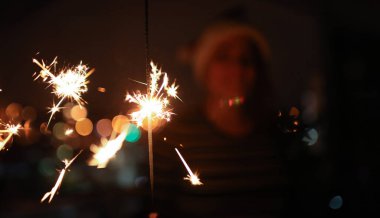 Yanan Bengal ışıklarına yakın çekim. Gülümseyen kadın arka planda mutluluk ve hayranlıkla maytaplara bakıyor. Mutlu yıllar ve Mutlu Noeller konsepti