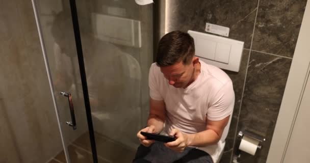 Der Mann Sitzt Auf Der Toilettenschüssel Und Spielt Ein Spiel — Stockvideo