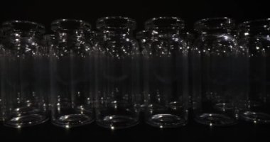 Aşılar için tasarlanmış şeffaf cam şişeler koyu arka planda duruyor. Tıbbi amaçlar için profesyonel bir laboratuvar malzemesi.