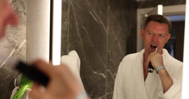 Homem Casaco Branco Limpa Cuidadosamente Dentes Com Escova Dentes Elétrica — Vídeo de Stock