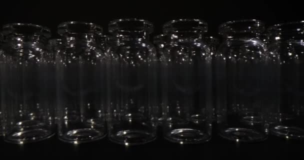 ワクチン用に設計された透明なガラス製バイアルは暗い背景で列に並んでいます 医療目的のための専門研究室用ガラス製品 — ストック動画