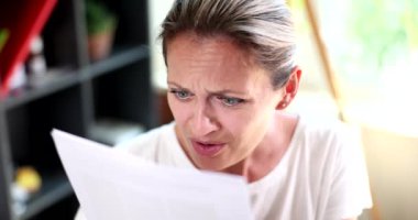 Portrait of woman who looks inquiringly and displeasedly at credit document. Woman with poor eyesight trying to read letter