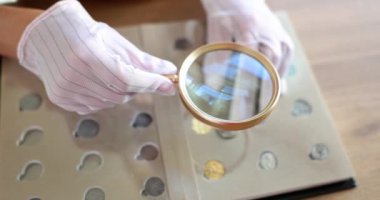 Numismatist examines coin from ancient collection. Catalog of coins by numismatics