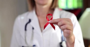Red ribbon as symbol of fight against HIV in hands of doctor. World AIDS Day and medical care