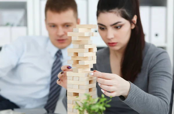 Businessman and businesswoman plays in strategy hand rearranging wooden blocks involved during break at work in office sitting table gaming pile fun joy pastime concept.