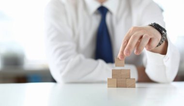 İşadamı elinde tahta küpü tutuyor ve piramit gibi duruyor. Küçük ve orta büyüklükte işletme geliştirme kavramı