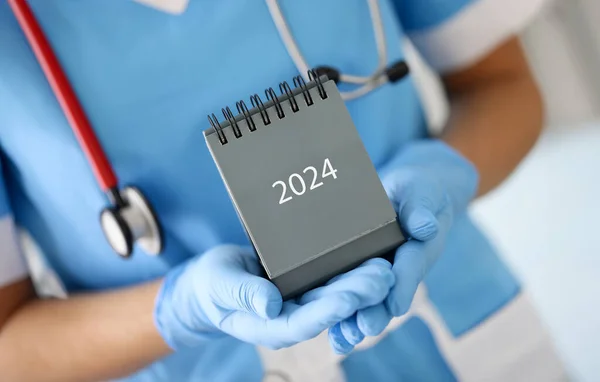 Doctor in medical rubber gloves holding desk calendar for 2024 closeup. Work schedule of medical staff concept